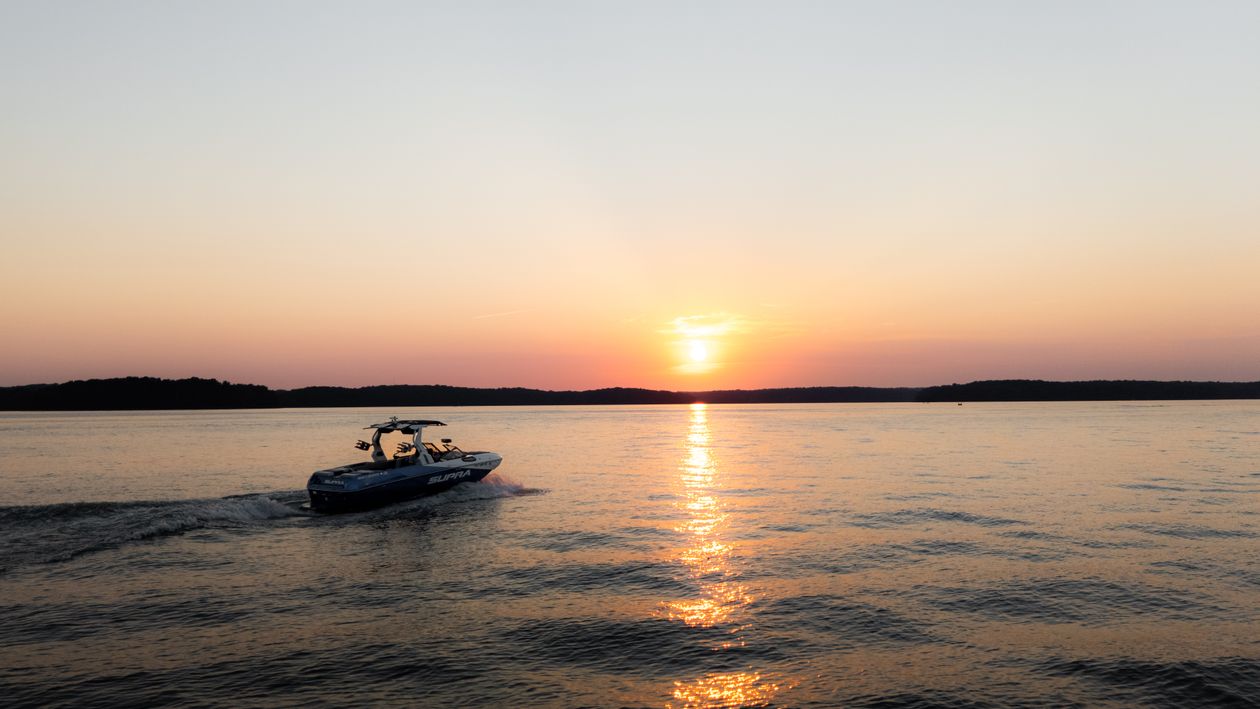 Wake boat cruising across a lake at sunset